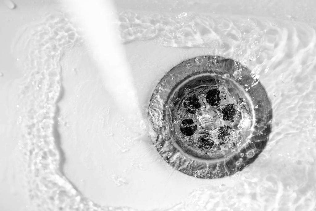 A stream of clean water flows into the drain hole of a white sink with a shallow depth of field